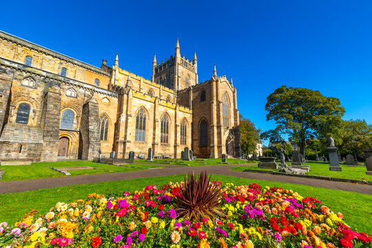 Dunfermline Abbey stands tall with colorful flowers in front during sunny weather in Dunfermline, Fife, Scotland, United Kingdom