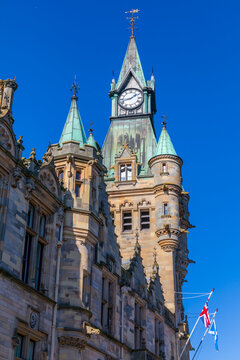 Clock Tower rises above Dunfermline City Chambers in Fife, Scotland with blue sky and flags visible