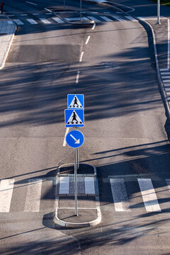 Empty urban road in Stockholm, Sweden meets a crosswalk, traffic island and signs while lane shadow patterns stretch across the asphalt