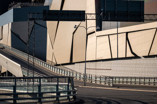 Sunlit urban architecture curves above an empty road in Stockholm, Sweden where ramp and railing lines define facade shadow and geometry