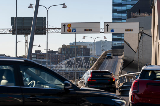 Traffic moves through Stockholm, Sweden toward a bridge beneath road signs, cars and urban architecture as light cuts across a commuter route