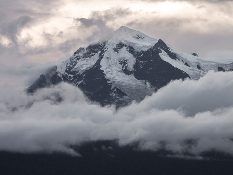 Sharp snowy Kawagebo peak in the Meili range at dawn with clouds wrapping around the mountain in soft light