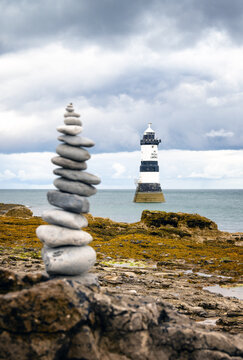 Stone tower stands in front of Trwyn Du Lighthouse in Anglesey, Wales under cloudy sky