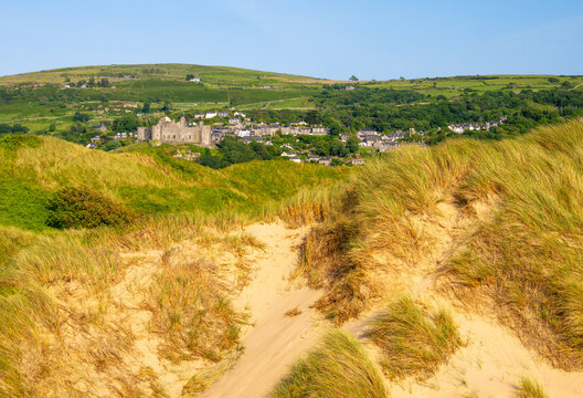 Sand dunes and Harlech Castle visible in background with town of Harlech nestled in hills during clear weather in Gwynedd