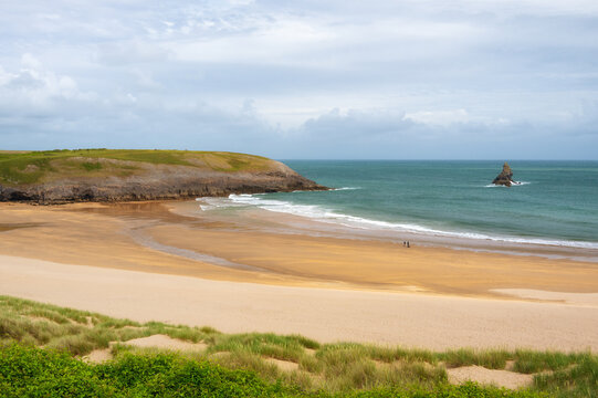 Couple walks with dog past Church Rock on Broad Haven South beach in Pembrokeshire