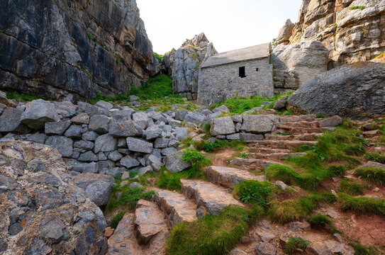 St Govans Chapel sits against a limestone cliff with steps leading to the entrance in Pembrokeshire, United Kingdom