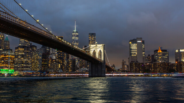 Brooklyn Bridge at dusk with city lights reflecting off the East River in New York City
