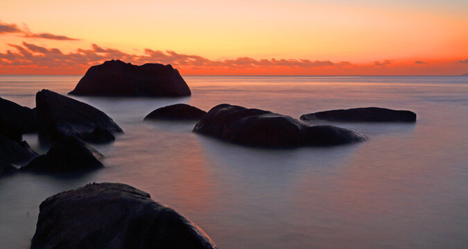 Sunset over calm waters with large rocks at Beau Vallon beach in Seychelles