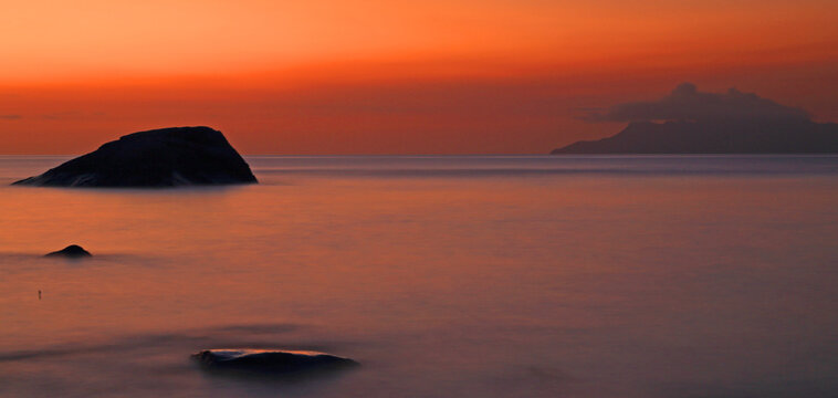Sunset over Beau Vallon beach with rock formations and distant land in the Seychelles