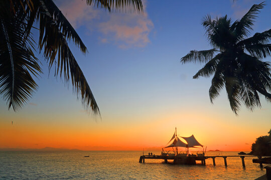 Beautiful sunset over the ocean near Coco de Mer hotel in Seychelles with silhouettes of palm trees and a wooden pier