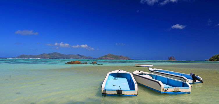 Boats anchored at Anse Source dArgent beach under sunny skies with turquoise waters and distant islands in Seychelles