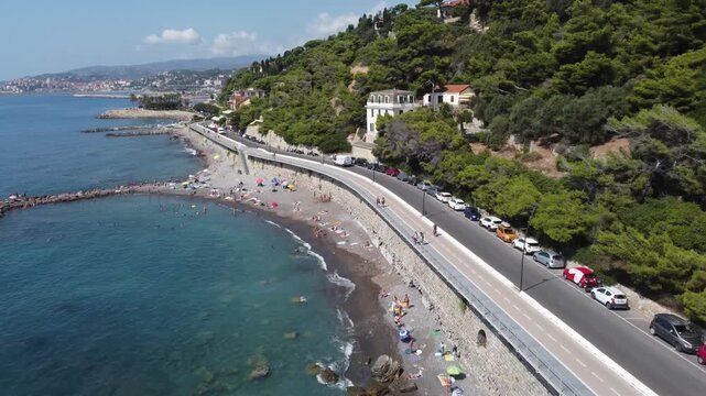 Aerial view of the coastline with people on the beach and cars parked along the road Imperia, Liguria, Italy.