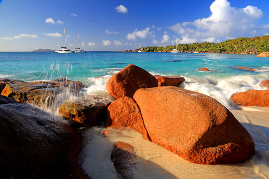 Bright water splashes at rocks along the shore near sailboats on a tropical beach in Seychelles