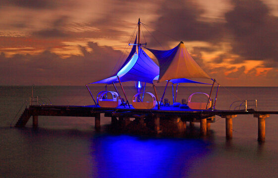 View of sunset at Coco de Mer resort with lit structures on the pier at Praslin Island in Seychelles