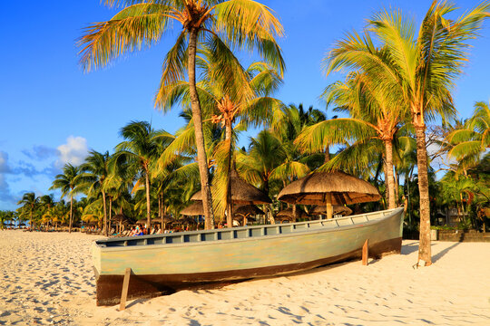 Visitors enjoy the beach at Pointe aux Piments in Mauritius with palm trees and a boat on the shore during sunset