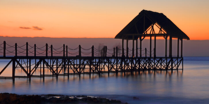 Sunset view over a wooden pier with a thatched roof on the coast of Mauritius