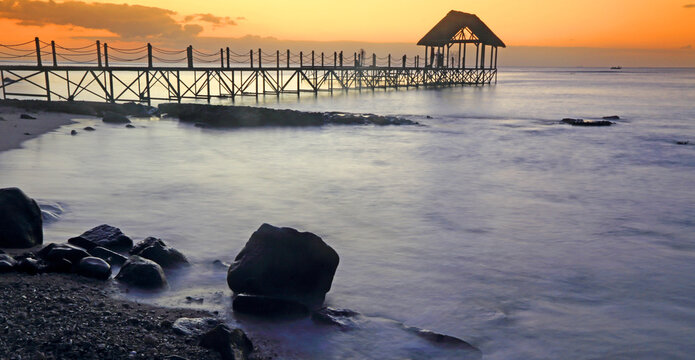 Sunset view over a pier with rocks and water in the foreground at Pointe aux Piments in Mauritius during evening hours