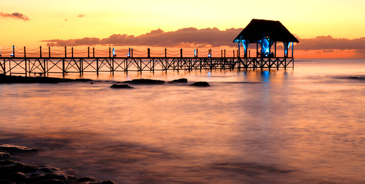 Sunset view over a wooden pier with calm water at Pointe aux Piments in Mauritius