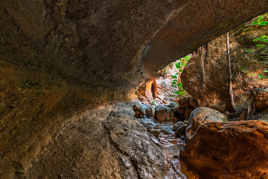 Water flows under a natural stone arch in Barranco de Luna gorge in Granada, Andalusia, Spain, showing rocky formations and vegetation
