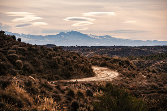Winding dirt road through arid hills leading to mountains in the background in Granada, Andalusia, Spain