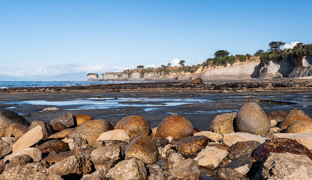 Coastal boulders and limestone cliffs by the ocean under clear skies in New Zealand offer a view of nature's beauty