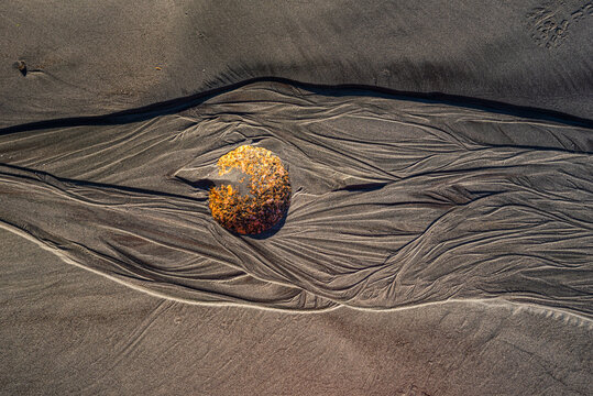 Rounded stone sits in rippled sand at Cape Foulwind Beach on the West Coast of New Zealand in bright sunlight during low tide