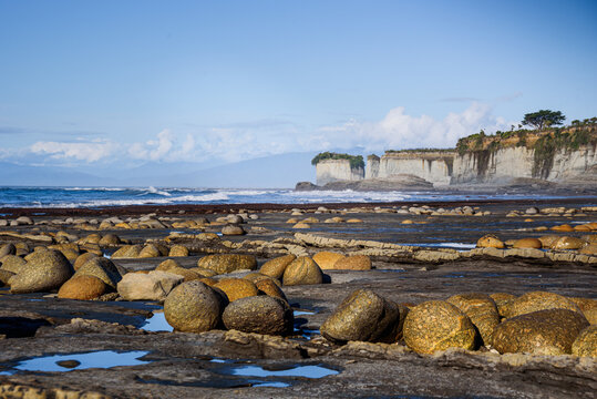Eroded coastal formations at low tide reveal unique rock patterns and pools along the shoreline in New Zealand