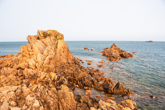 Golden light shines on coastal rocks at Lions Rock in Guernsey during sunset over the Atlantic Ocean