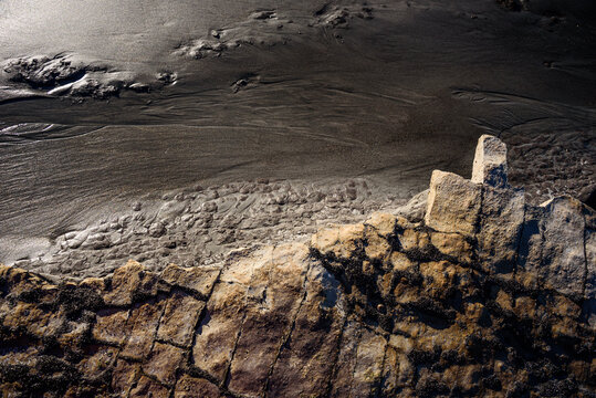Weathered sandstone forms and dark sand contrast at a coastline in New Zealand