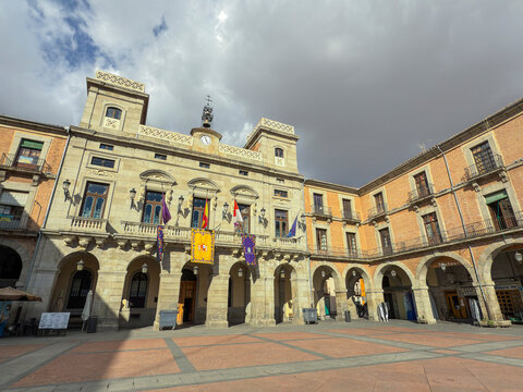 Town Hall building at Plaza del Mercado Chico during a cloudy day in Avila, Extremadura, Spain with visitors and flags displayed