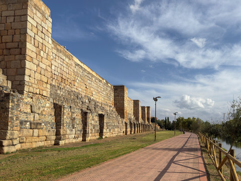 City walls stand along the promenade by the Guadiana River in Merida, Extremadura, Spain under a blue sky with clouds
