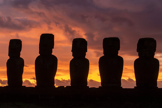 Sunrise silhouettes of moai at Ahu Tongariki on Easter Island in Chile with orange and purple sky