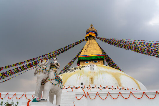 Visitors gather near Boudhanath Stupa while colorful prayer flags flutter on a cloudy day in Kathmandu, Nepal