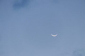 Fototapeta premium Crescent moon blue sky twilight cloud evening minimalism celestial astronomy Soft glowing crescent moon clear blue twilight sky with faint cloud