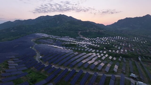 Aerial view of a mountainous photovoltaic power station at sunset with solar panels arranged in neat rows