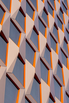 Orange shadow traces geometric panels across an abstract architecture facade where pattern and building detail turn exterior cladding into a graphic study