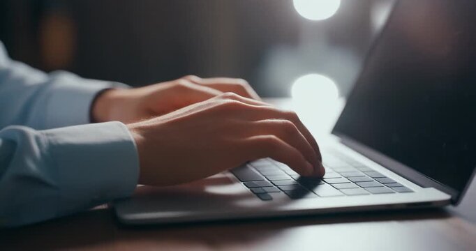 Business professional typing on laptop keyboard at office desk during night time.