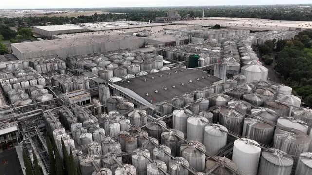 Extensive industrial tank farm with silver wine storage containers at Gallo Winery in Modesto, California, with processing facilities during overcast day in United States. Aerial flyover.