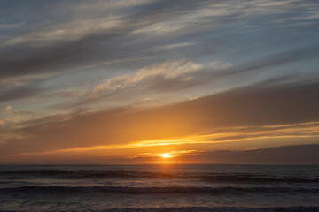 Obraz premium Golden sunset over the ocean with dramatic clouds and gentle waves
