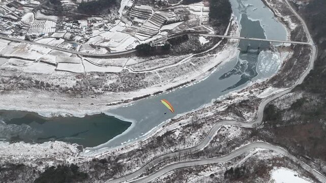Paragliders over snow-covered landscape and frozen river