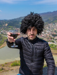 Obraz premium Georgian man in a papakhi with a glass of wine. Selective focus.
