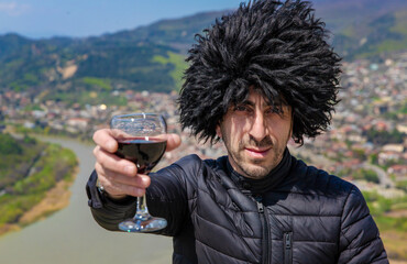 Obraz premium Georgian man in a papakhi with a glass of wine. Selective focus.