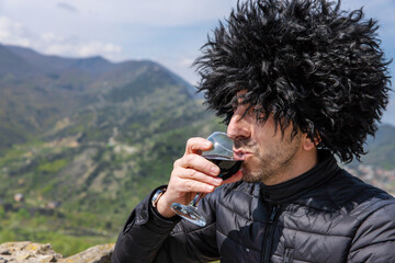 Obraz premium Georgian man in a papakhi with a glass of wine. Selective focus.