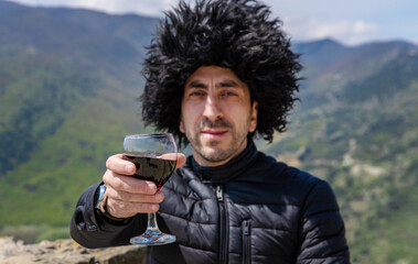 Obraz premium Georgian man in a papakhi with a glass of wine. Selective focus.