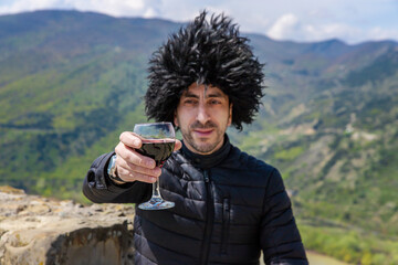 Obraz premium Georgian man in a papakhi with a glass of wine. Selective focus.