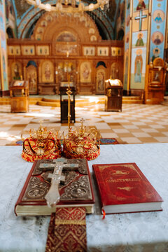Orthodox wedding ceremony attributes in church interior: golden crowns, holy bible with cross, and prayer book on altar table. Vertical composition with soft light.