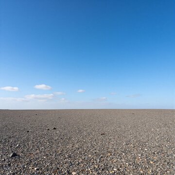 Vast expanse of a pebble beach under a clear blue sky with scattered clouds