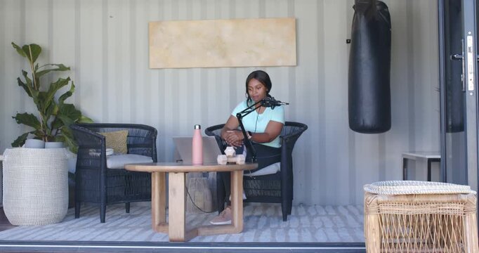 African American woman on patio checking laptop and starting podcast, speaking into boom mic