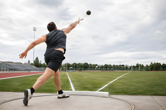 Male Shot Put Athlete Competing on Outdoor Athletics Field Under Cloudy Sky
