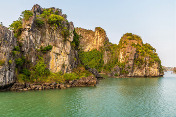 Fototapeta premium A view from a cruise ship into a lagoon surrounded by Karst limestone cliffs in Ha Long Bay, Vietnam illuminated by the evening light